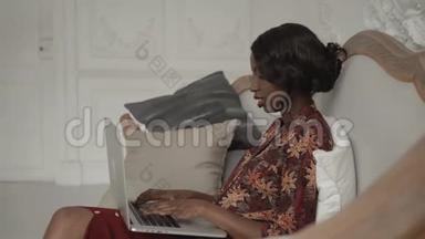 用电脑躺在沙发上笑非裔美国学生女人